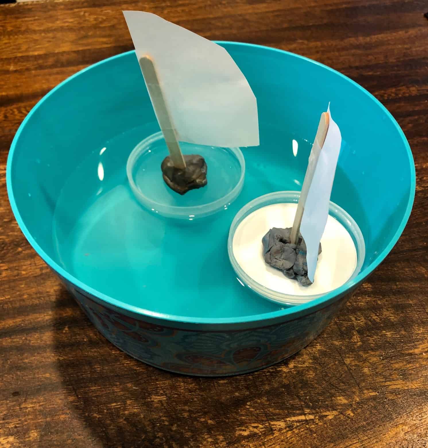 little boats made from repurposed containers, play dough, popsicle sticks, and paper floating in a large container