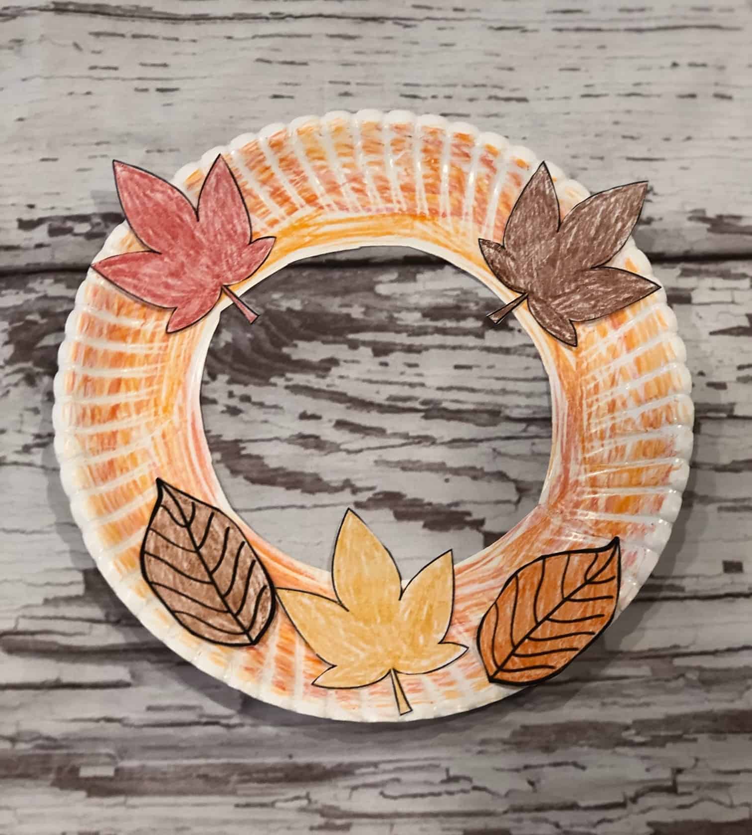 a paper plate wreath with leaves glued on it. It is is fall colored (orange, yellow, brown)