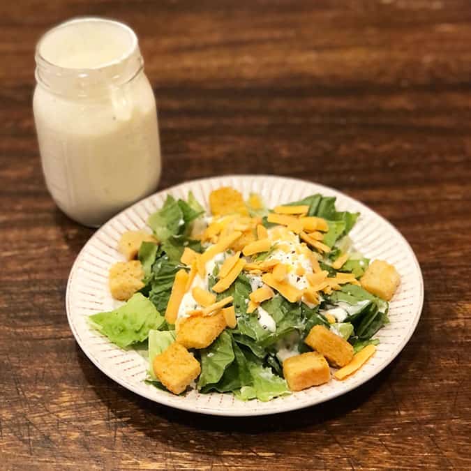 A green salad with croutons, cheese, and ranch. There is also Copycat Outback Ranch Dressing in a mason jar in the background. 