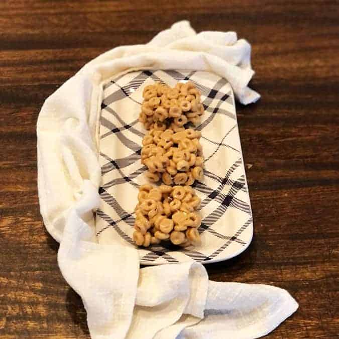 Peanut Butter Cheerio Bars on a black and white plate surrounded by a cream colored linen.
