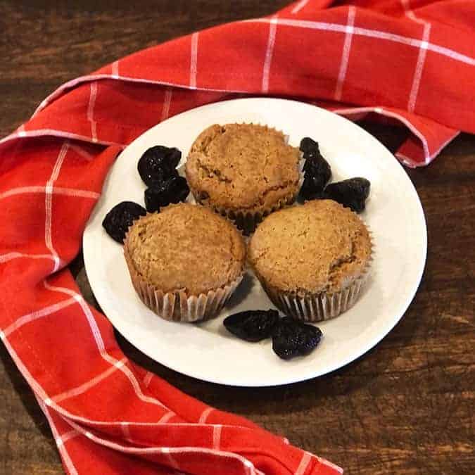 Prune Muffins surrounded by prunes on a white plate with a red linen.