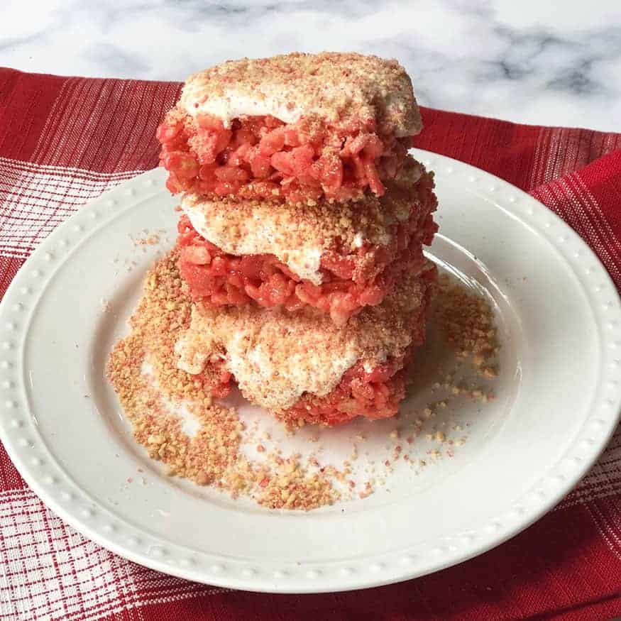 Strawberry Rice Crispy Treats with frosting and strawberry crunch crumble stacked together on a plate.