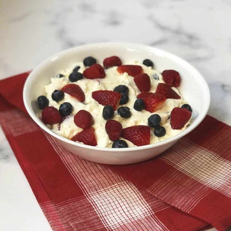 Triple Berry Cheesecake Fruit Salad in a white bowl with a red linen under it. 