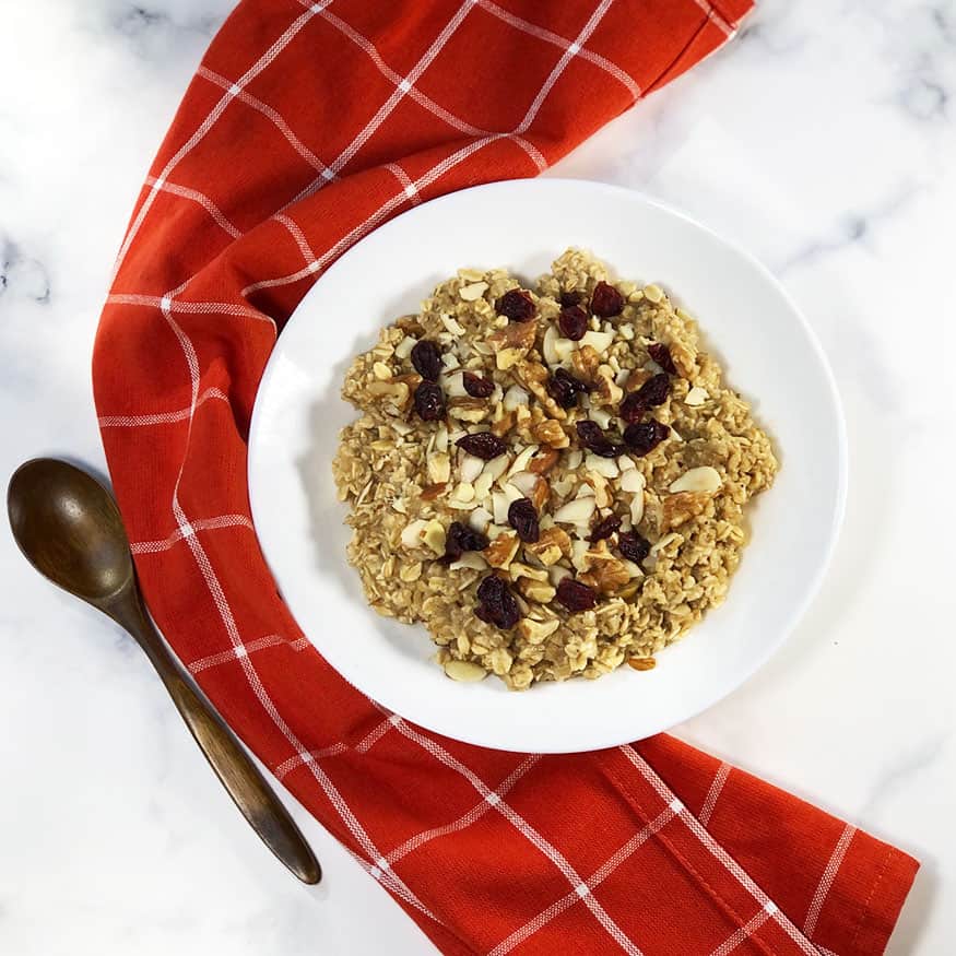 Copycat Starbucks oatmeal (oatmeal with craisins, almond slices and walnuts) in a white bowl with a wooden spoon and red linen.