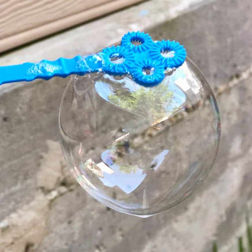 A bubble hanging from a blue bubble wand. 