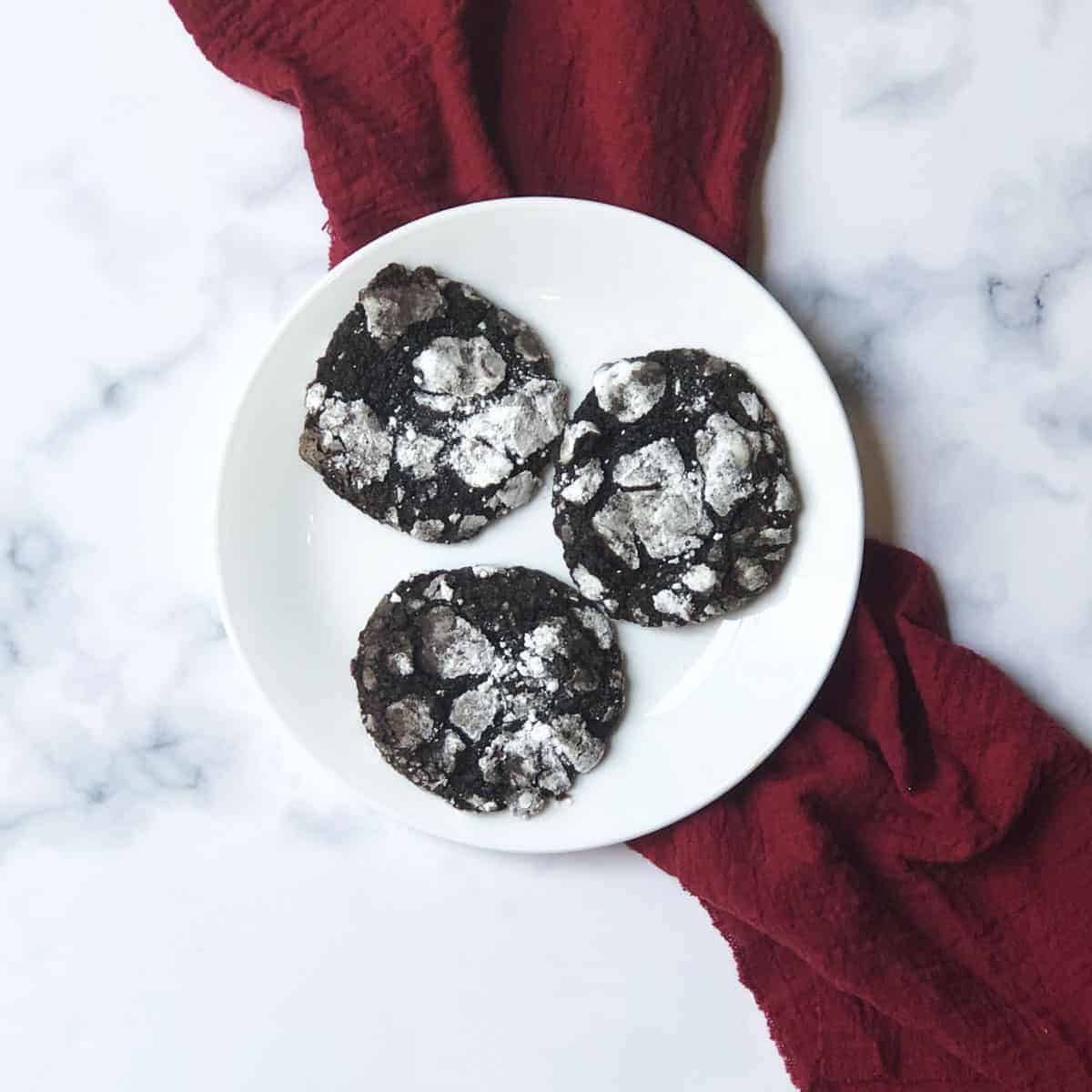 Chocolate crinkle cookies on a white plate with a red linen. 