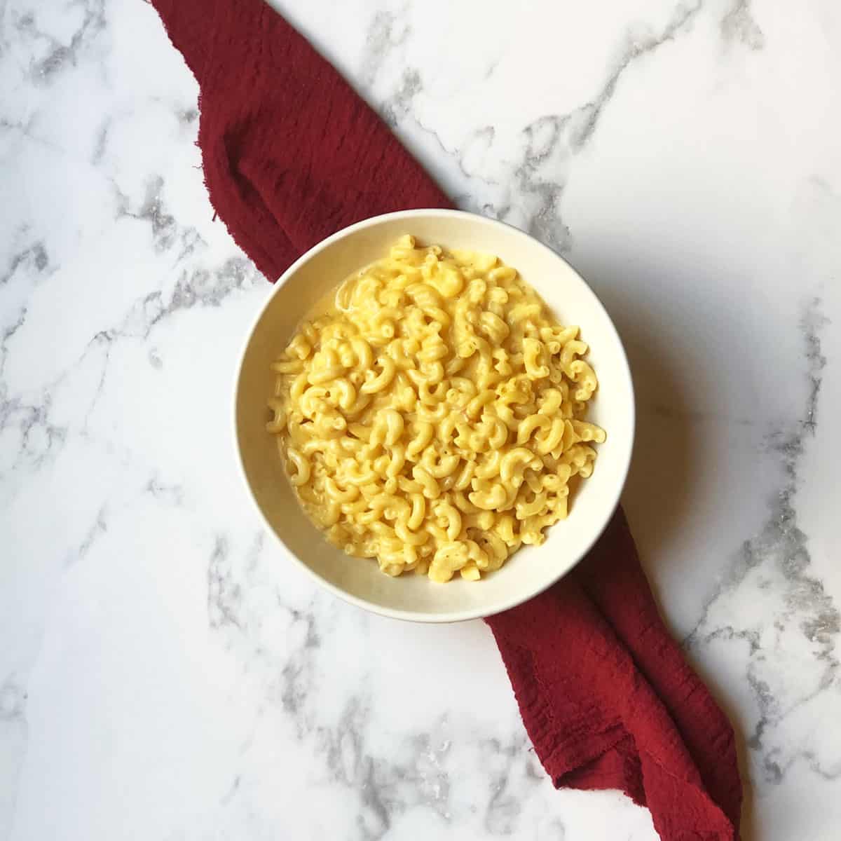 A bowl of macaroni and cheese with a red linen under it. 