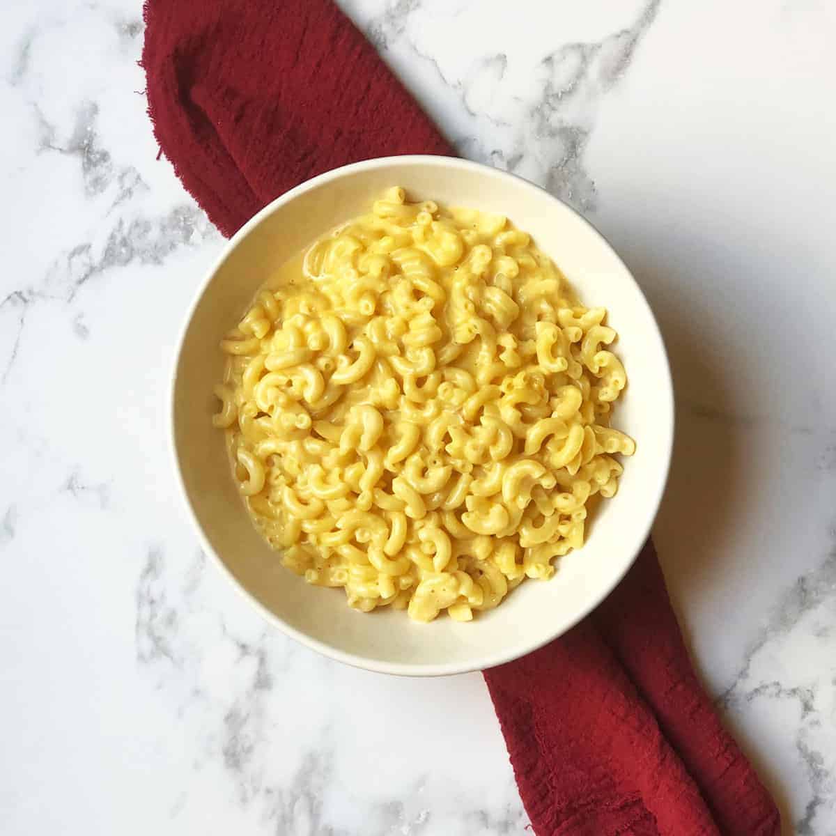 A bowl of macaroni and cheese with a red linen under it. 