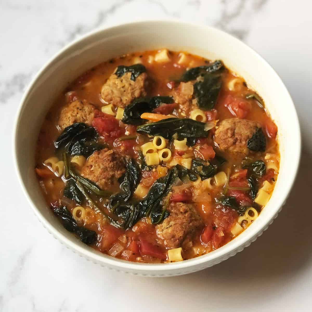 Lactation Soup (soup with spinach, meatballs, and pasta) in a white bowl