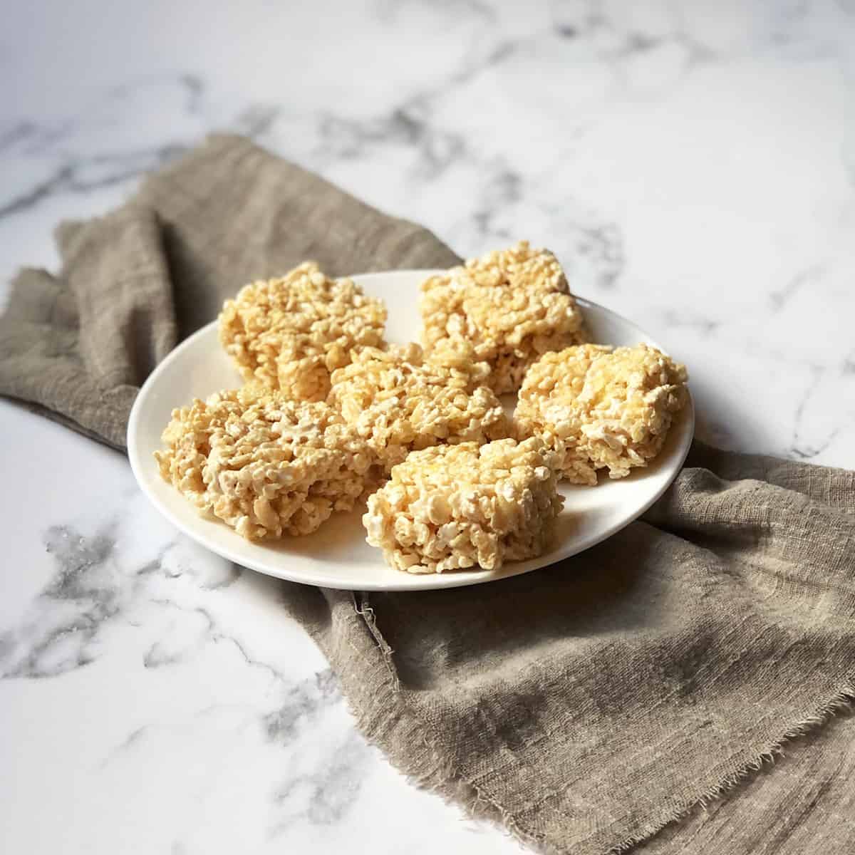Some rice crispy treat squares on a white plate with a gray linen. 