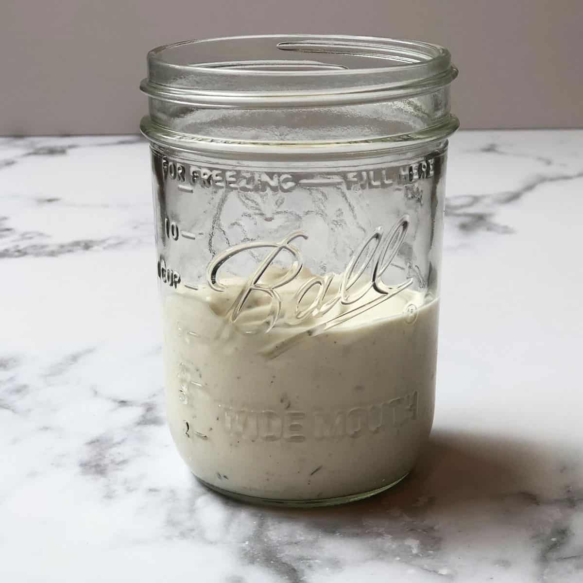 A mason jar filled with ranch in it. 