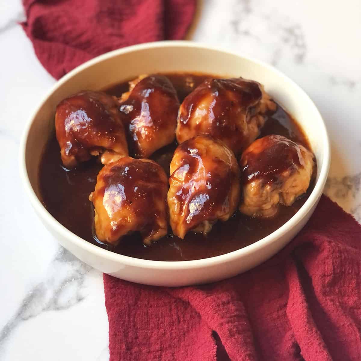 BBQ chicken thighs in a white bowl with a red linen.