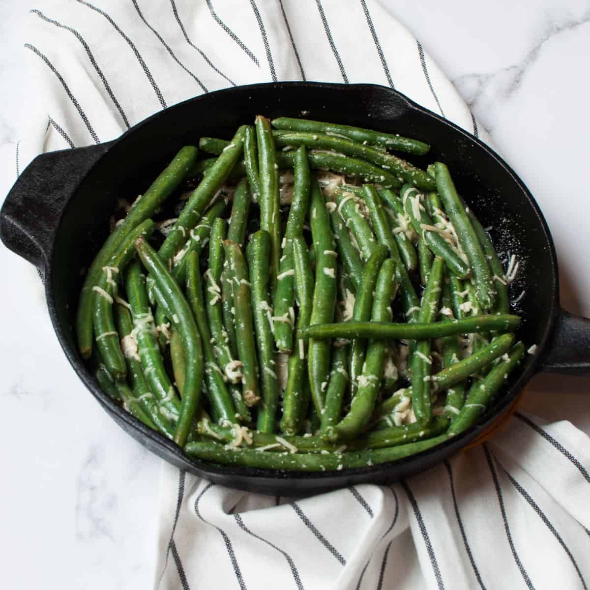 Upclose photo of green beans in a cast iron skillet with a striped linen