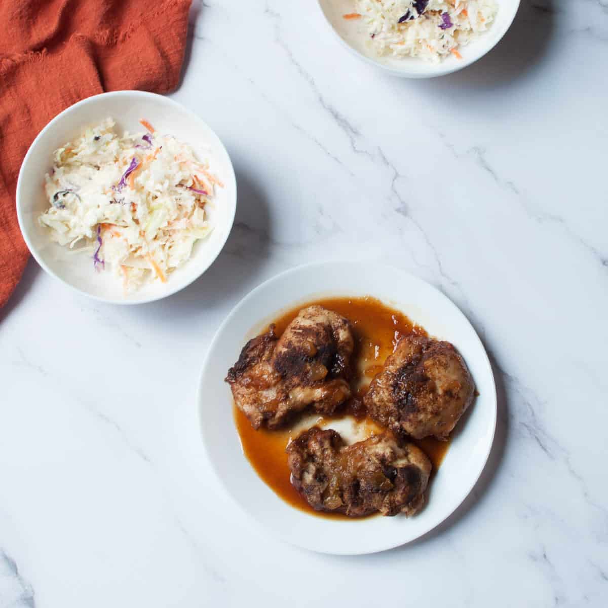 plate of Instant Pot Hawaiian Chicken Thighs there are bowls of coleslaw in the background
